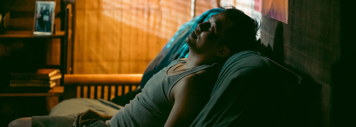 A man with a bruised face sits on a couch in a dimly lit apartment